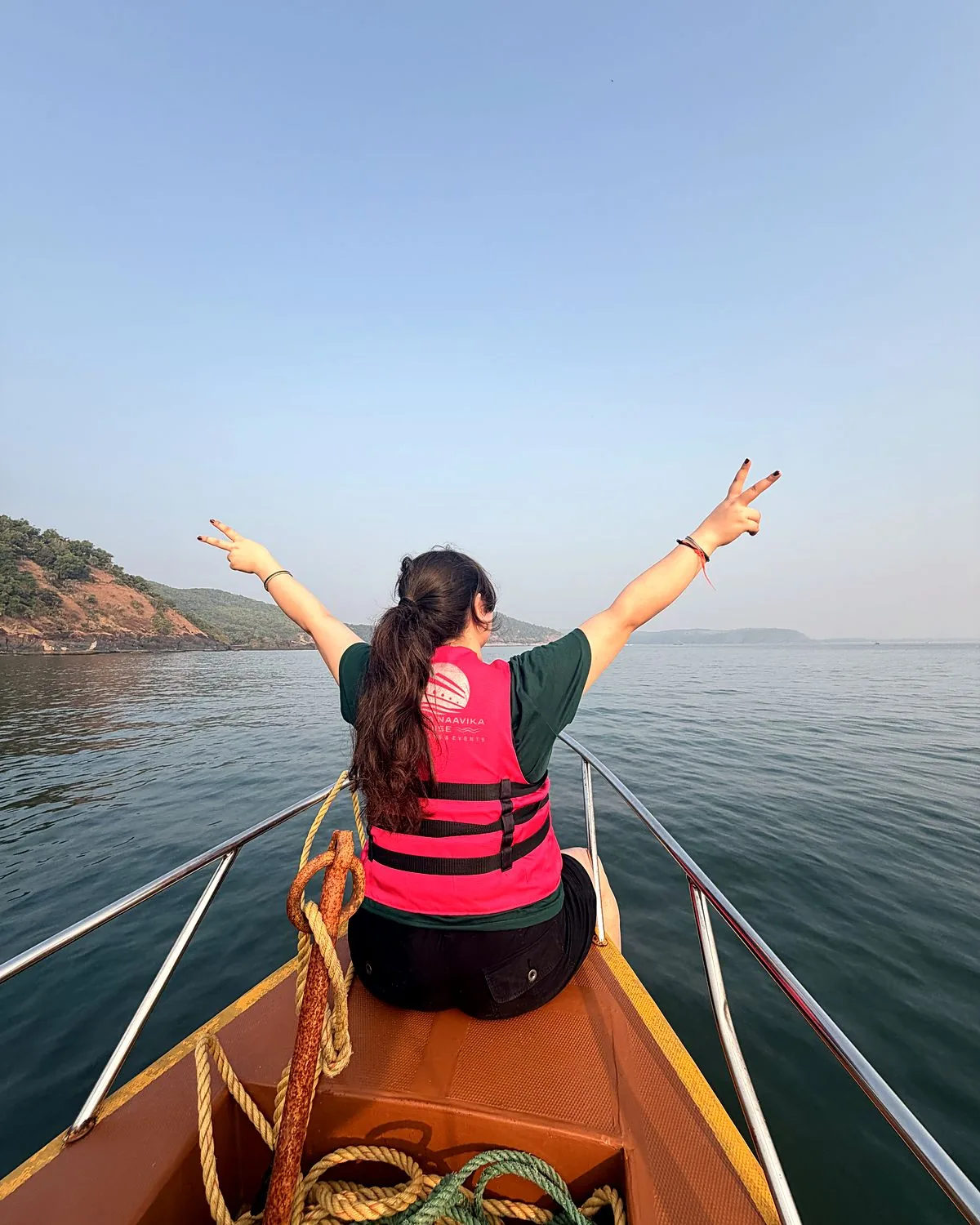 Guest with arms raised at the bow of a Naavika boat, Gokarna coast ahead