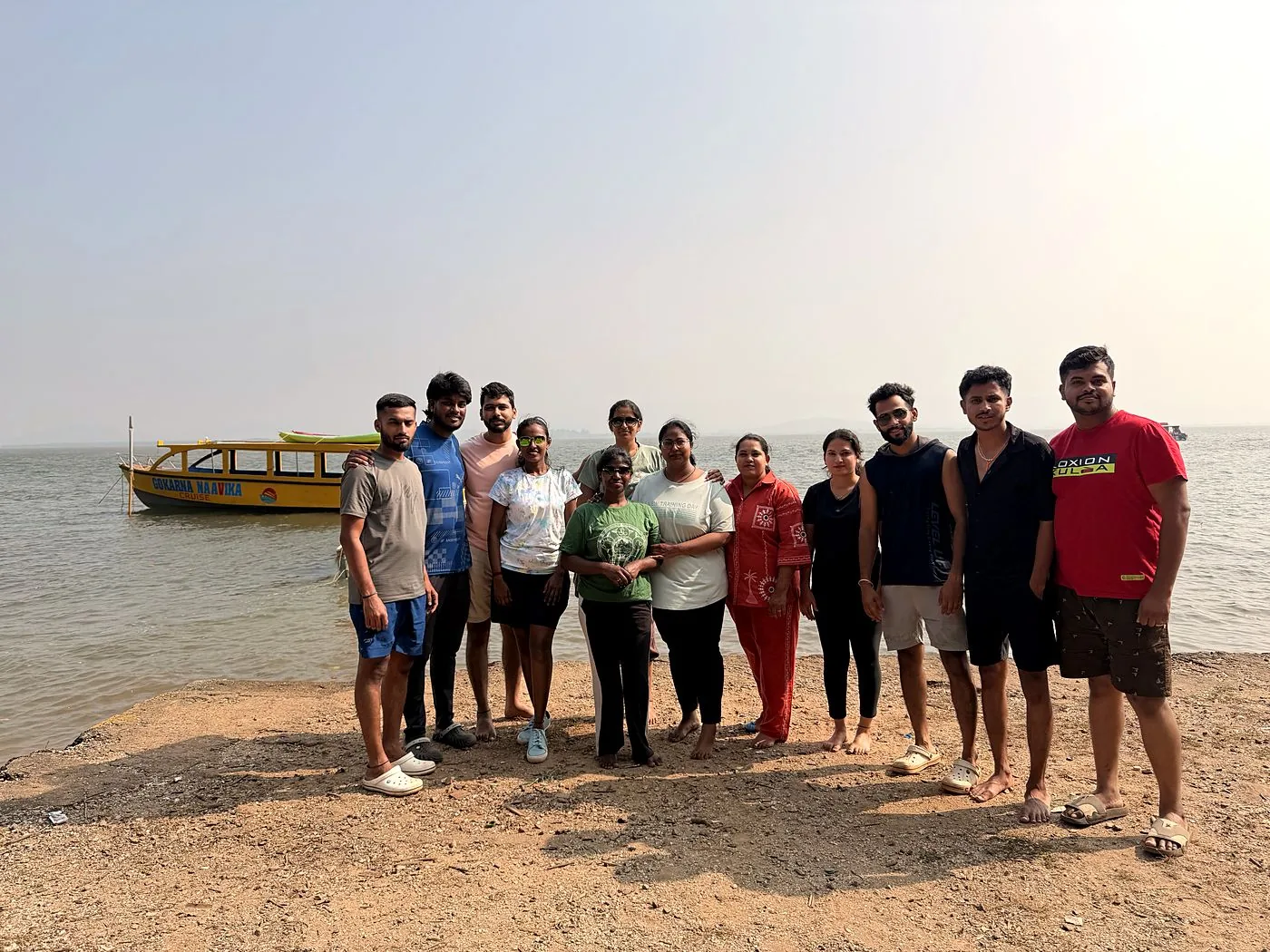 Group of travellers on a Gokarna beach with the Naavika boat offshore